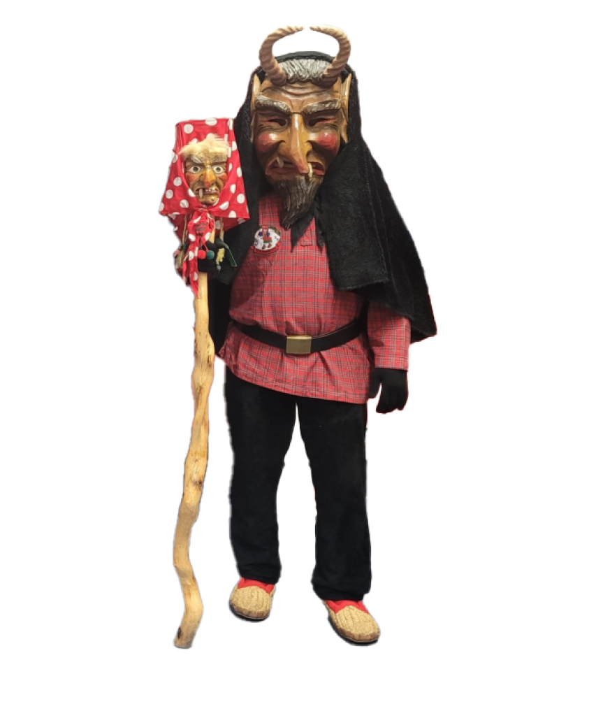 Person in traditioneller Tracht mit rotem Hemd, schwarzer Hose, Strohsandalen und Hörnern auf dem Kopf, hält einen Stab mit rotem Tuch und Kerze.