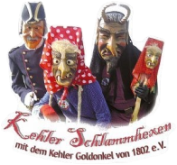 Drei Personen in traditionellen Kostümen, eine mit rotem Kopftuch und Maske, Text 'Kehler Schlawumhexen mit dem Kehler Goldonkel von 1802 e.V.'